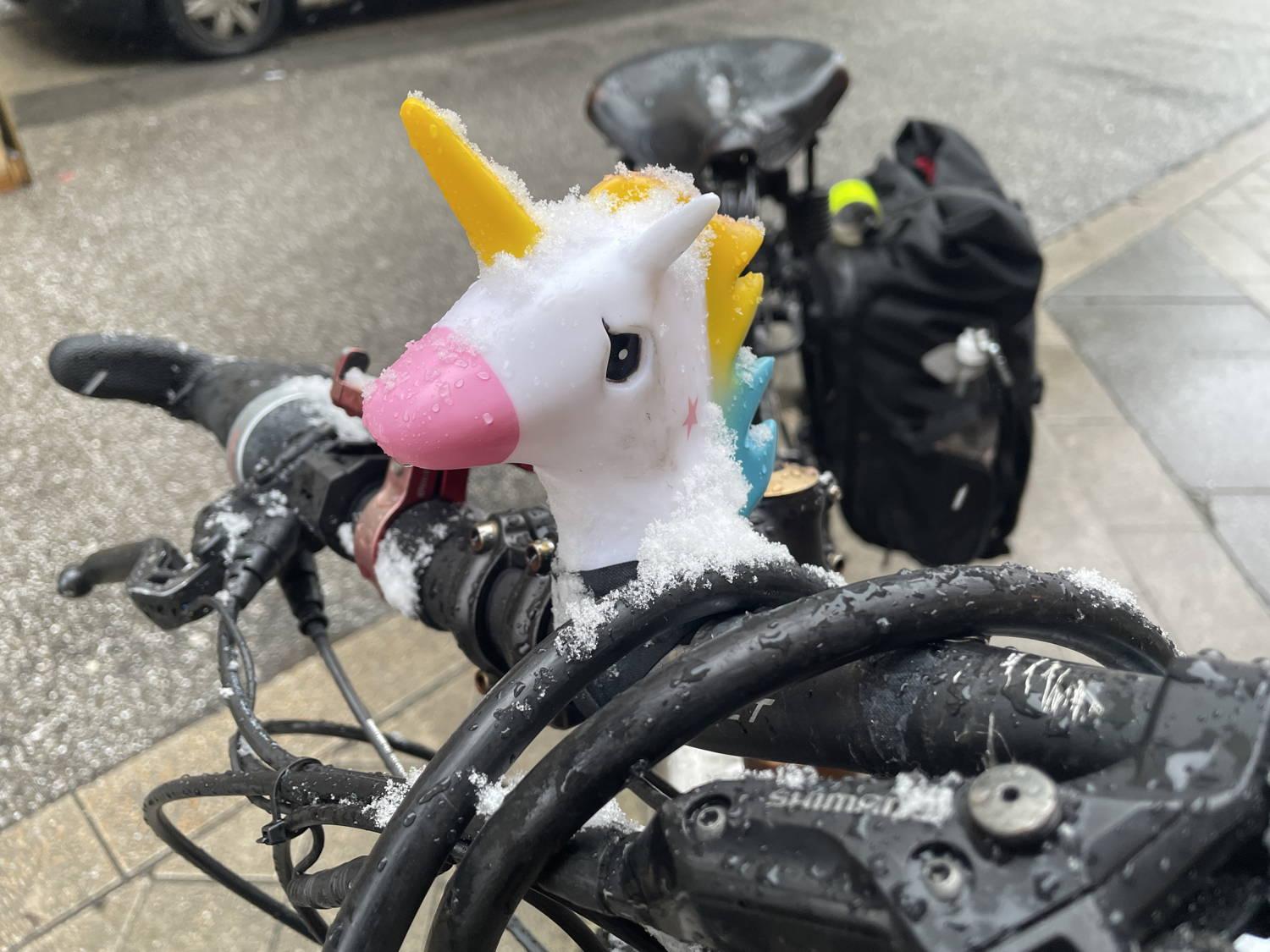 eine Fahrradhupe un Form eines Einhornkopfes ist an einem Fahrradlenker montiert. Auf dem Lenker und dem Einhorn haben sich Eiskristalle abgelagert - das Gesicht der Figur sieht irgendwie traurig aus
