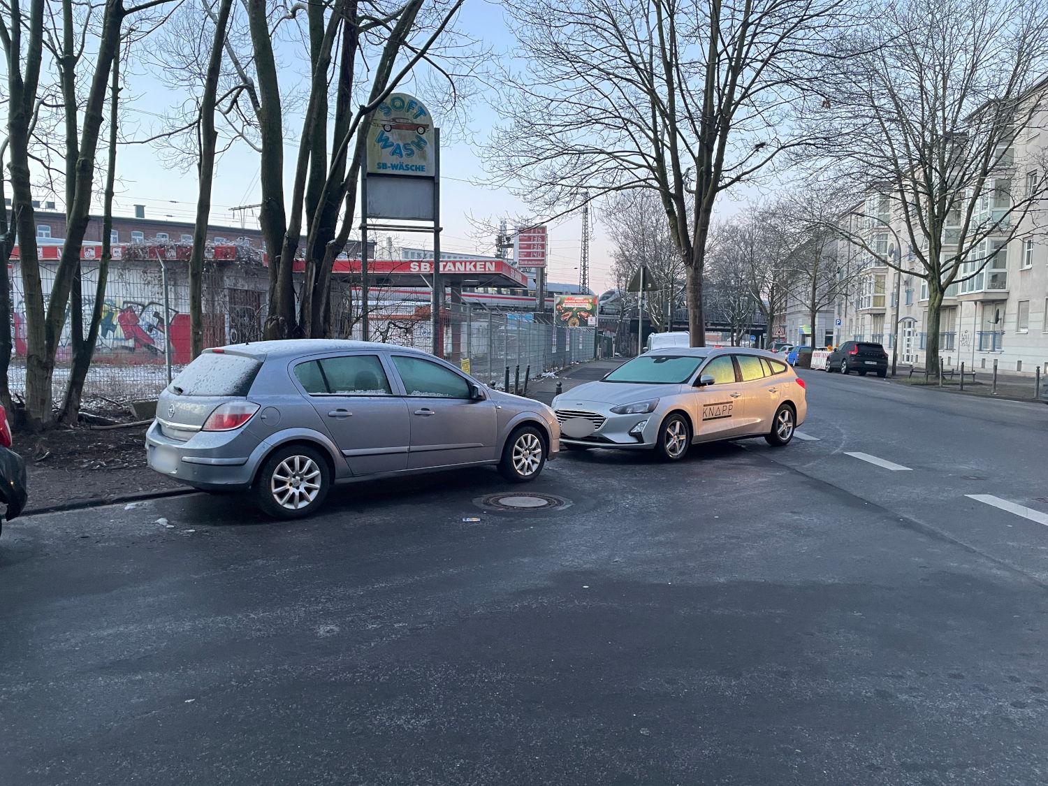 zwei Autos parken im Bereich einer Straßen-Einmündung so voreinander das der Fuss- und Radweg blockiert ist, das Heck des einen Wagens ragt in die Straße hinein von der die Einmündung abbiegt.