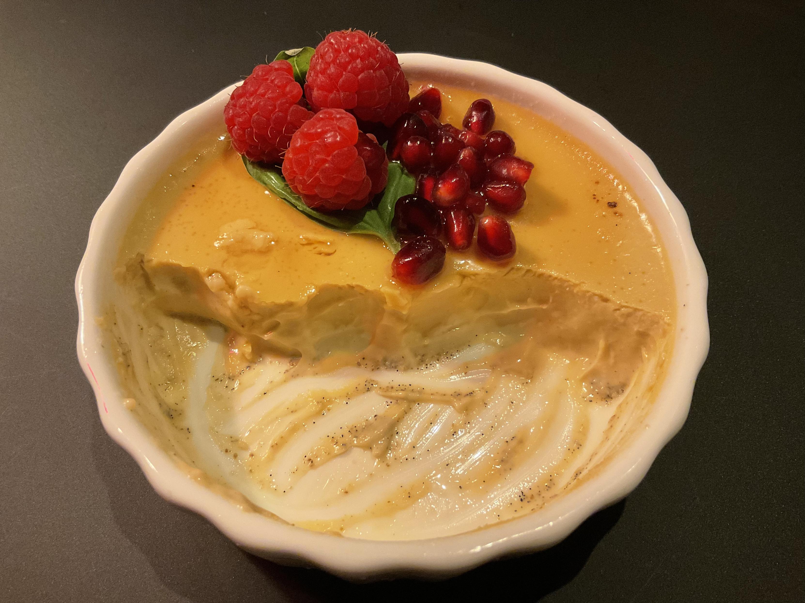 Dasselbe Schälchen, halb leergegessen, die Deko ist noch da.
Man sieht auf dem Boden des Schälchens, dort, wo die Creme weggegessen wurde, schwarze Vanillekörnchen.