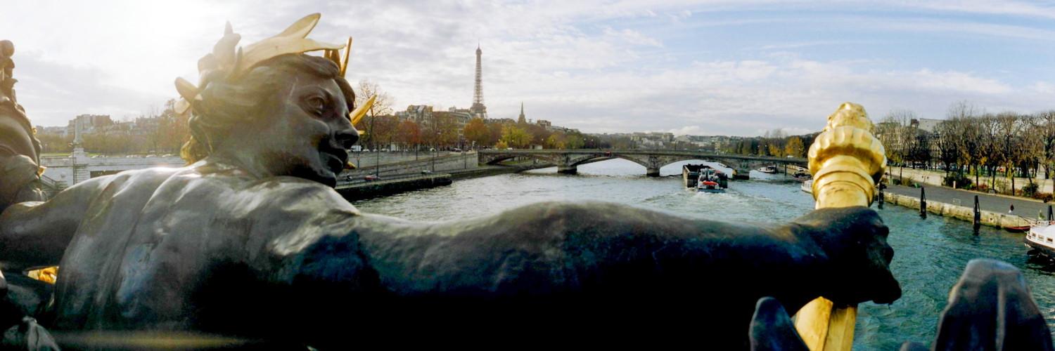 panoramic view showing the Seine and Paris. The camera is standing on a bridge and looking over the shoulder of a sculpture. It seems like the sculpture is embracing the whole city with its arms
