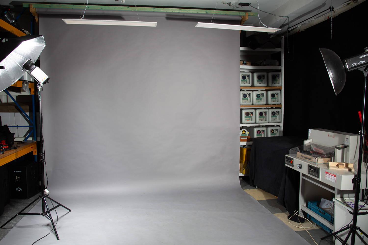 a grey backdrop is hanging from the roof and lying on the ground in a studio. on both sides of the backdrop there are two studio-flashes installed on tripod - they fired for this picture and give the illumination