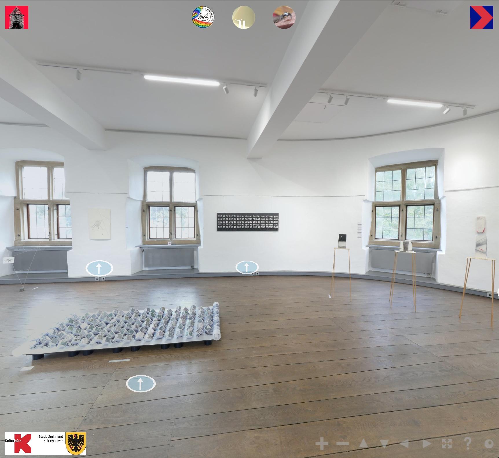 A room with white walls in which medieval windows are set. Green foliage can be seen through the windows. The room has a wooden floor made of thick dark brown planks. There are prints hanging at the walls and three-dimensional Installations visible in the room.