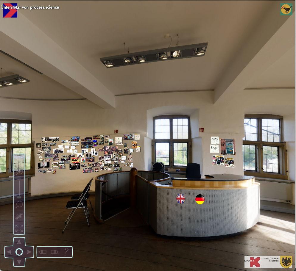 a medevial room with brown wooden floor an da round desk. There's a bunch of small pictures mounted on the walls