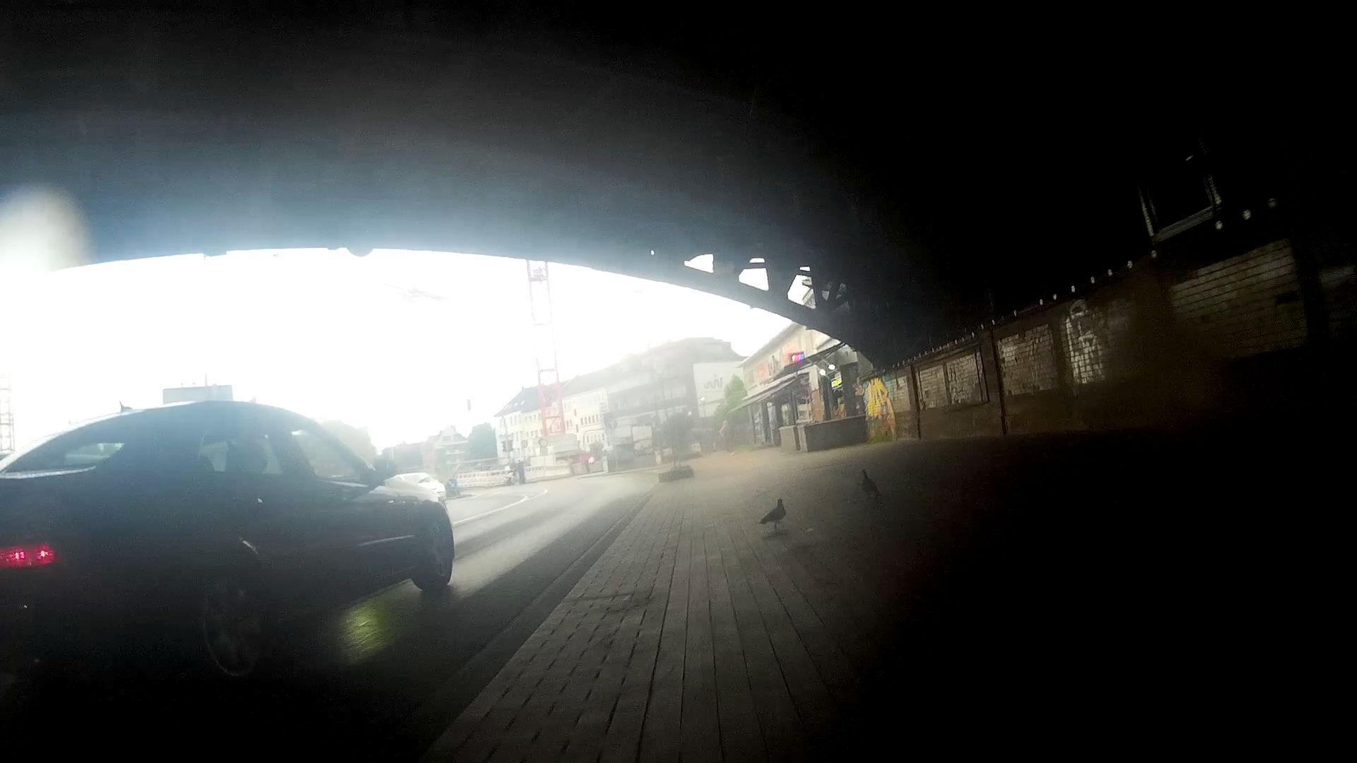 eine Bahnunterführung in Dortmund - das sogenannte Burgtor aus der Sicht einer Fahrrad-Dashcam aufgenommen. Man erkennt den Bogen der Brücke unter der die Straße verläuft, den Fuss/Radweg auf dem das Rad fährt und einen schwarzen Wagen der links neben dem Rad auf der Straße fährt